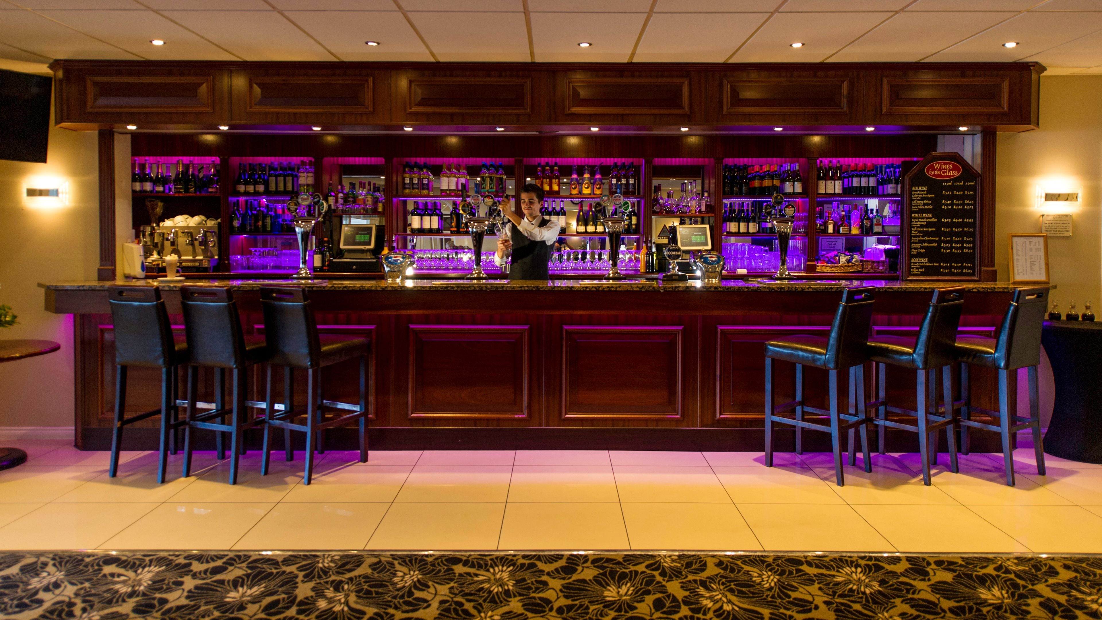 A bar with a wooden counter, multiple liquor bottles, and bar stools.