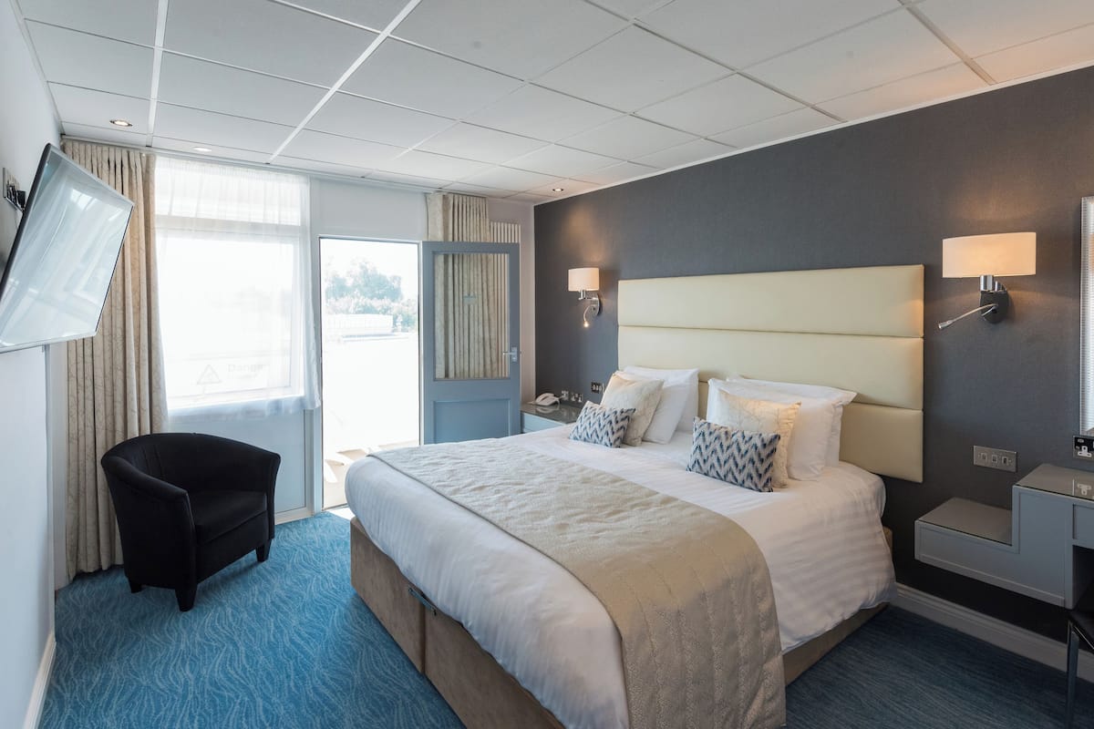 A hotel room with a large bed, a desk, a chair, a TV, and a bathroom with a mirror.