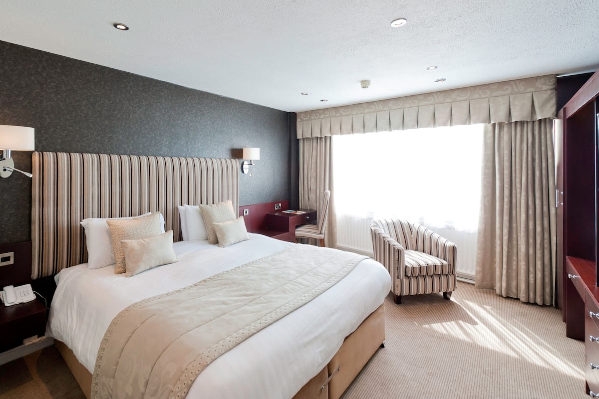 A hotel room with a large bed, a desk, a chair, and a window with curtains.