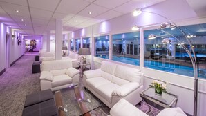 A hotel lobby with a pool view, white sofas, and a glass coffee table.