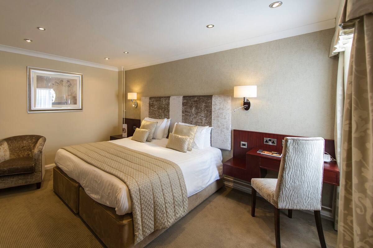 A hotel room with a large bed, a chair, a desk, and a TV mounted on the wall.