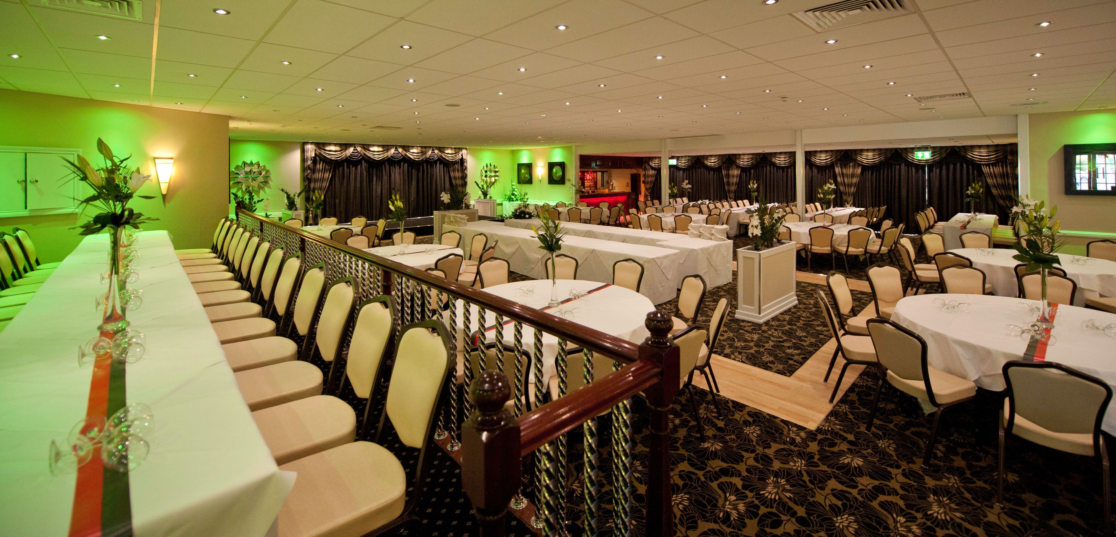 Un salón de banquetes con varias mesas redondas, sillas y un escenario.