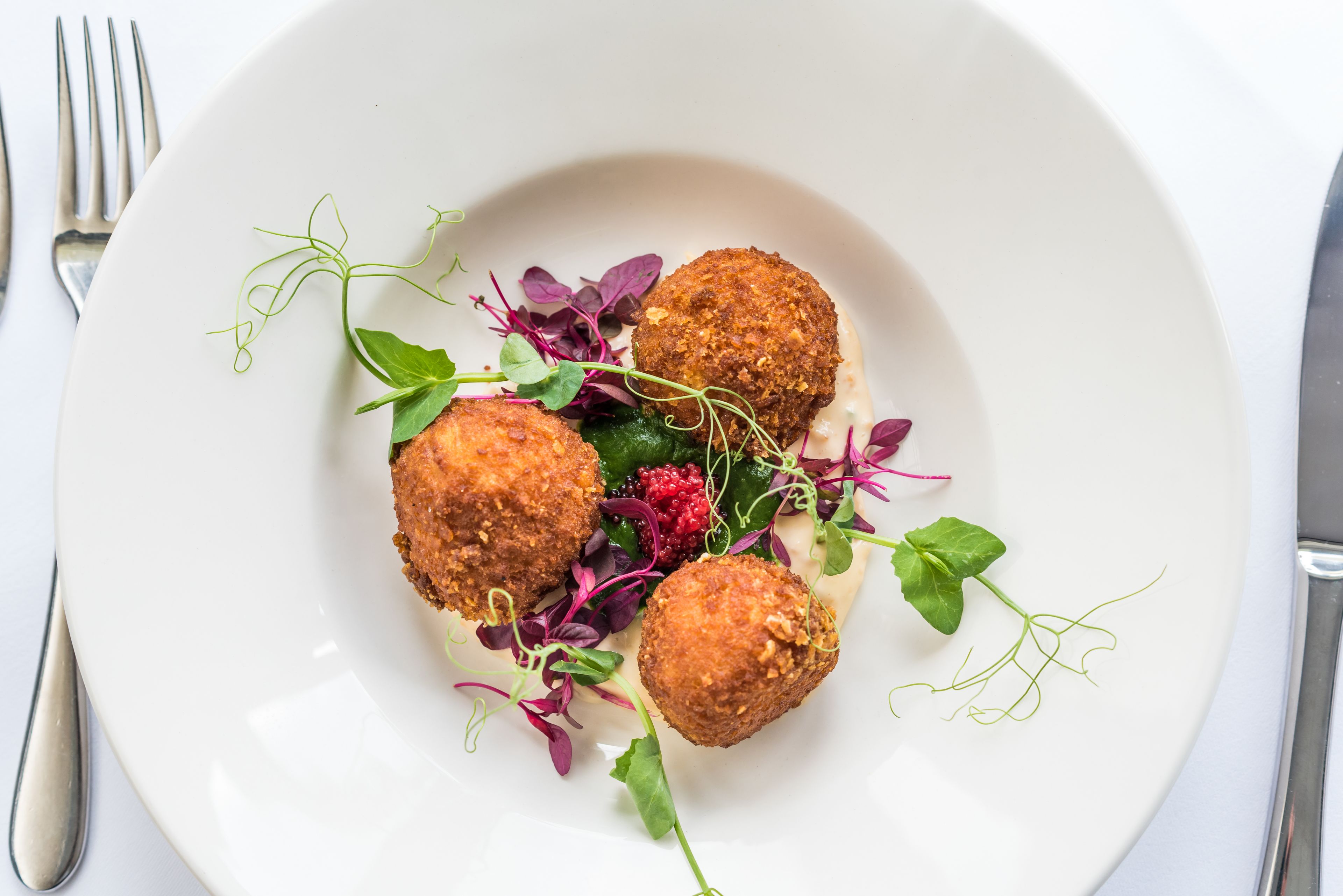 A white plate with three round, breaded items and a variety of greens and berries.