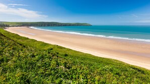 A coastal landscape with a sandy beach, grassy areas, and a clear blue sky.