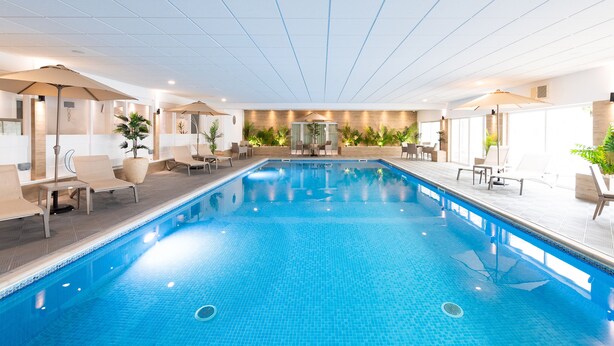 An indoor swimming pool with lounge chairs and umbrellas, surrounded by plants and modern decor.