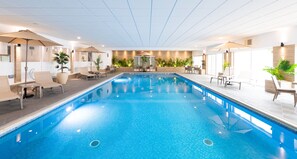 Una piscina interior con sillas de descanso y sombrillas, rodeada de plantas y decoración moderna.