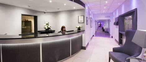 A reception area with a curved counter, a receptionist, a chair, and a hallway leading to a health club.