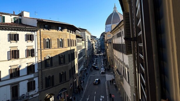 Vista callejera con edificios, cielo despejado y una estructura en forma de cúpula a lo lejos.