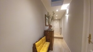 Un pasillo estrecho con un banco de madera, una puerta al final y un tragaluz en el techo.