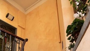 Una escalera con escalones oscuros y una barandilla de metal que conduce a una plataforma con una lámpara y una planta en maceta.