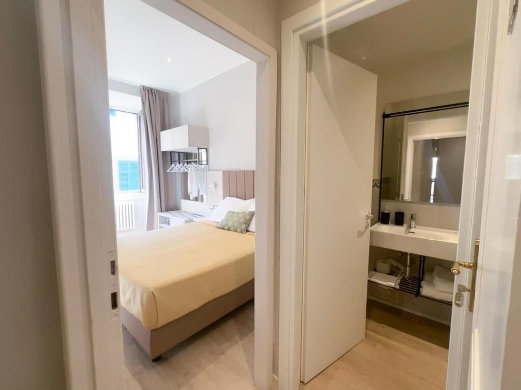 A hotel room with a bed, a bathroom with a mirror, and a view of the outside.