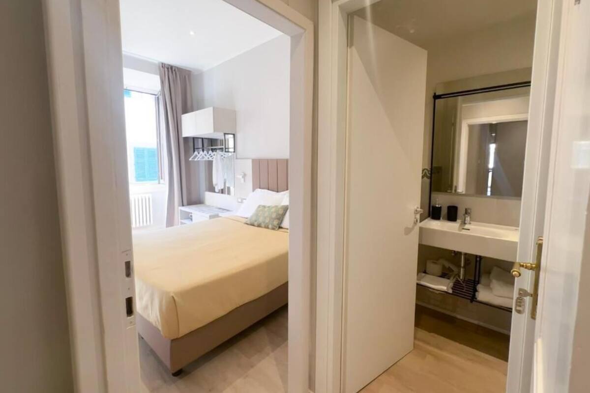 A hotel room with a bed, a bathroom with a mirror, and a view of the outside.