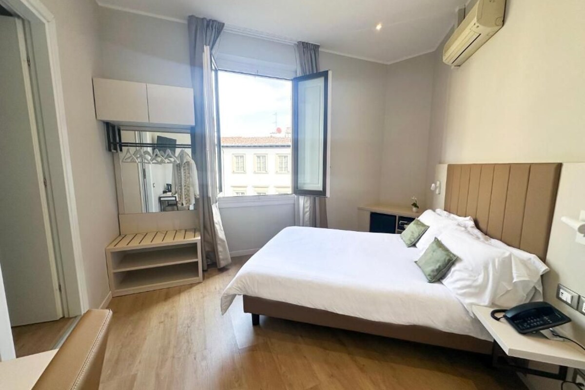 A hotel room with a bed, bedside table, and a window with curtains.