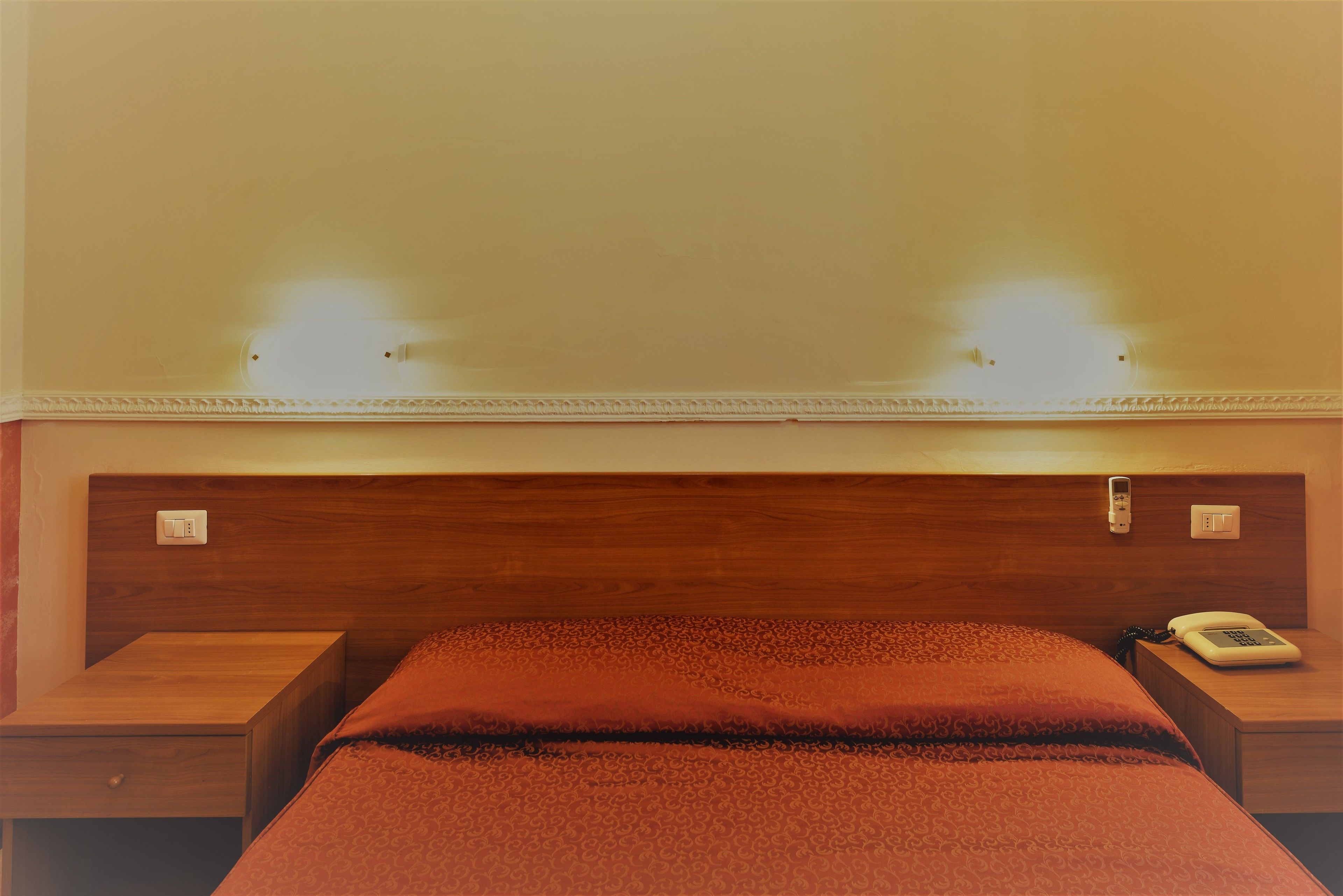 Camera d'albergo con una testiera in legno, un letto con copriletto rosso, due comodini e un telefono sul comodino.