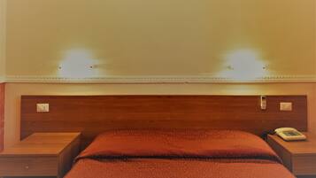 Camera d'albergo con una testiera in legno, un letto con copriletto rosso, due comodini e un telefono sul comodino.