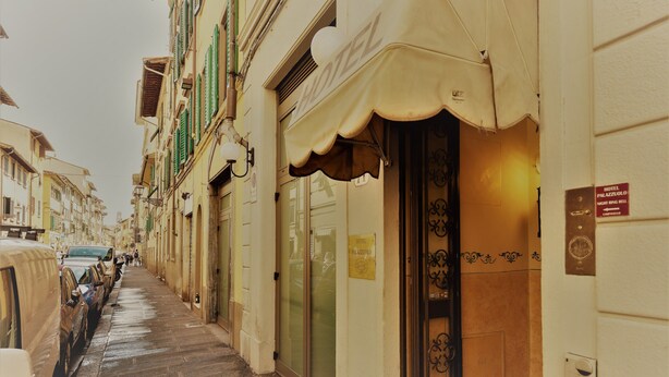 Una calle estrecha con coches estacionados y un hotel con un cartel que dice "HOTEL PALAZZOLO".