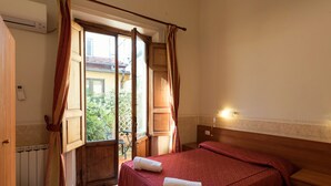 Un dormitorio con cama, mesita de noche, ventana con cortinas y vistas al exterior.