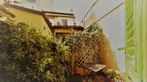Un pequeño patio al aire libre con una mesa y sillas, rodeado de follaje denso y una estructura de celosía de madera.