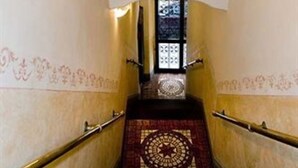 Una escalera con un mural de una figura musculosa sosteniendo una espada, barandilla y alfombra estampada.