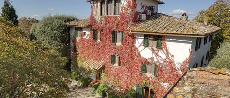 A traditional villa with a tiled roof, green shutters, and a garden with a seating area.