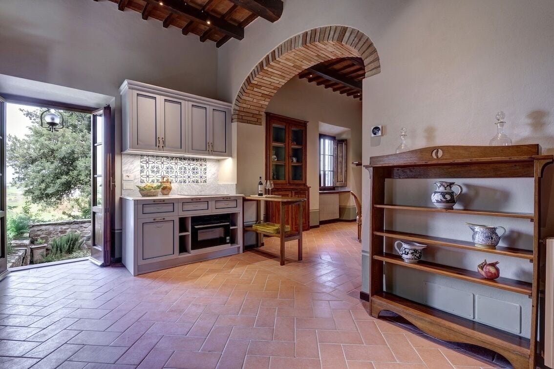 A kitchen with a herringbone floor pattern, a wooden cabinet, and a shelf with ceramic items.