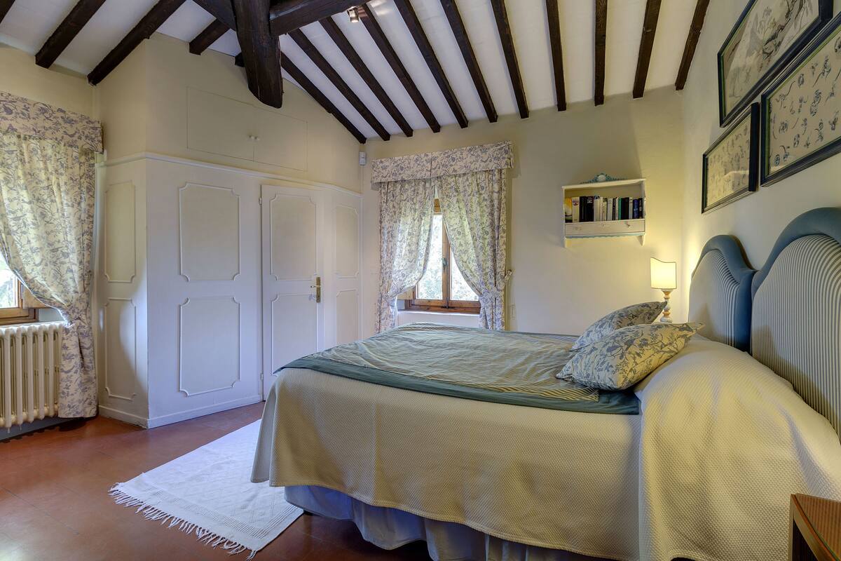 A bedroom with a bed, a window with curtains, a bookshelf, and a radiator.