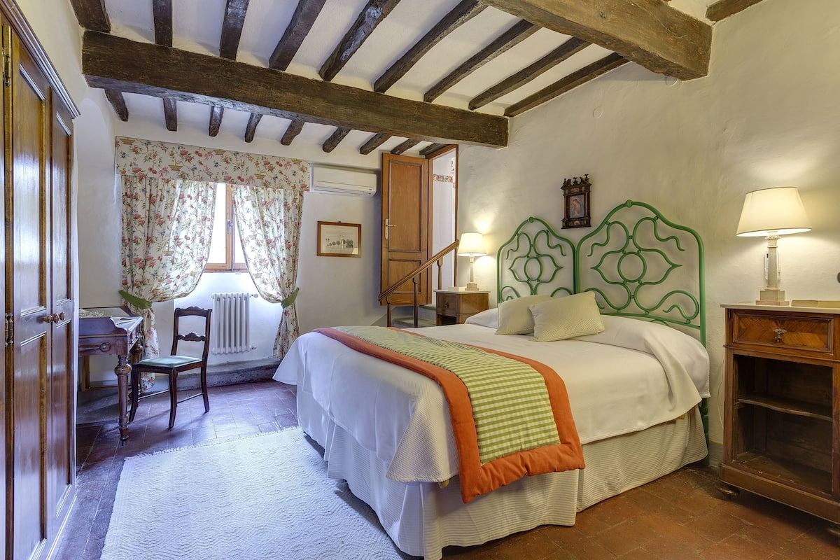A bedroom with a bed, wooden headboard, bedside tables, a desk, and a chair.
