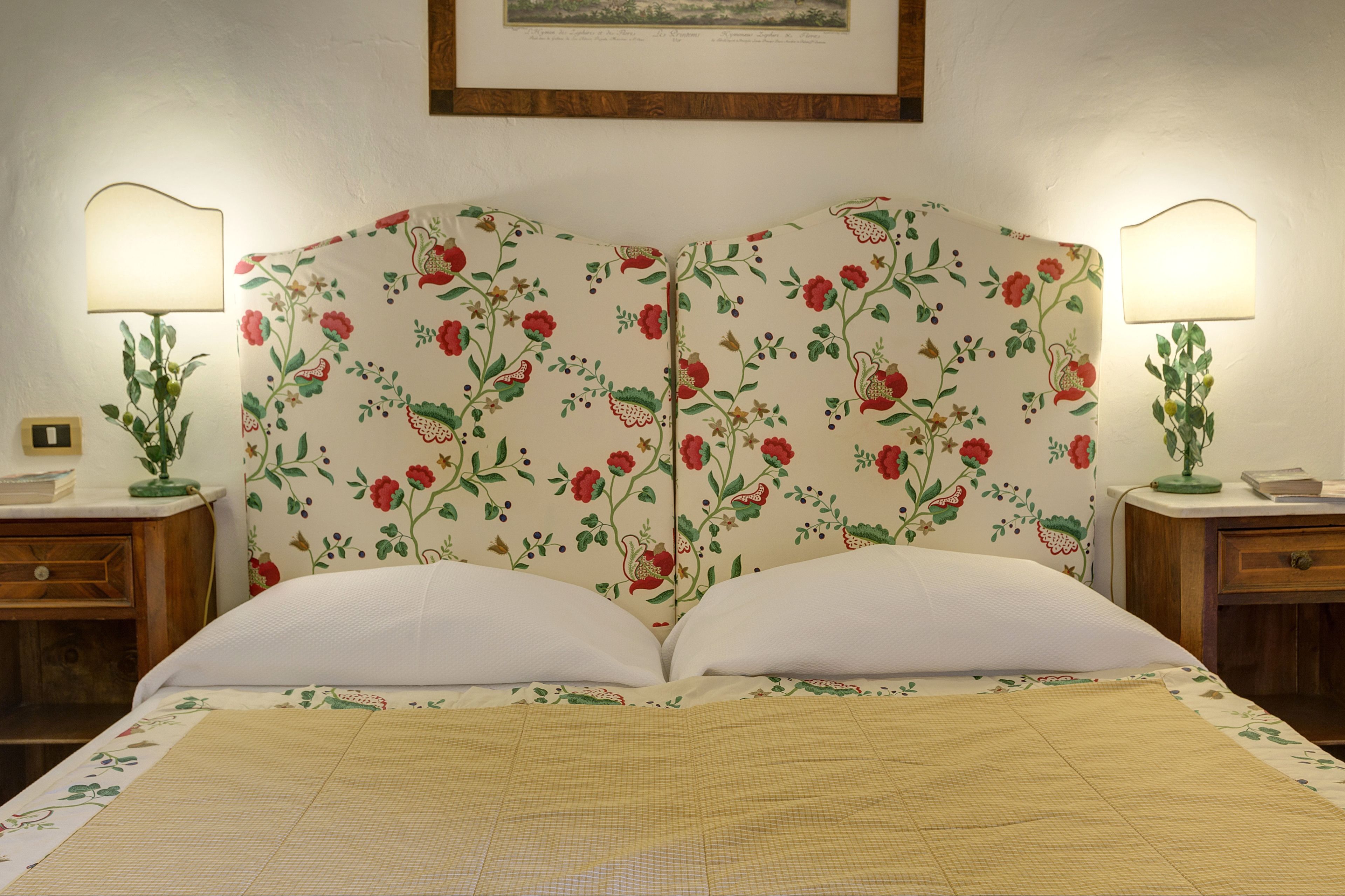 Una cama con cabecera estampada con motivos florales, dos mesitas de noche con lámparas y un cuadro enmarcado en la pared.