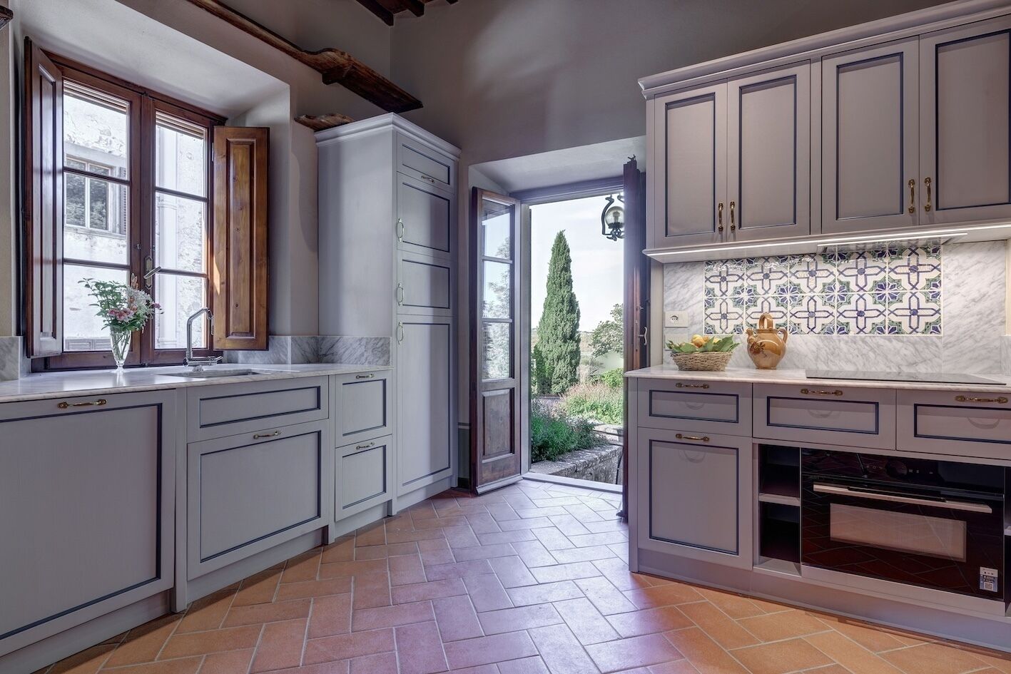 A kitchen with grey cabinets, a tiled backsplash, and a view of the outdoors.