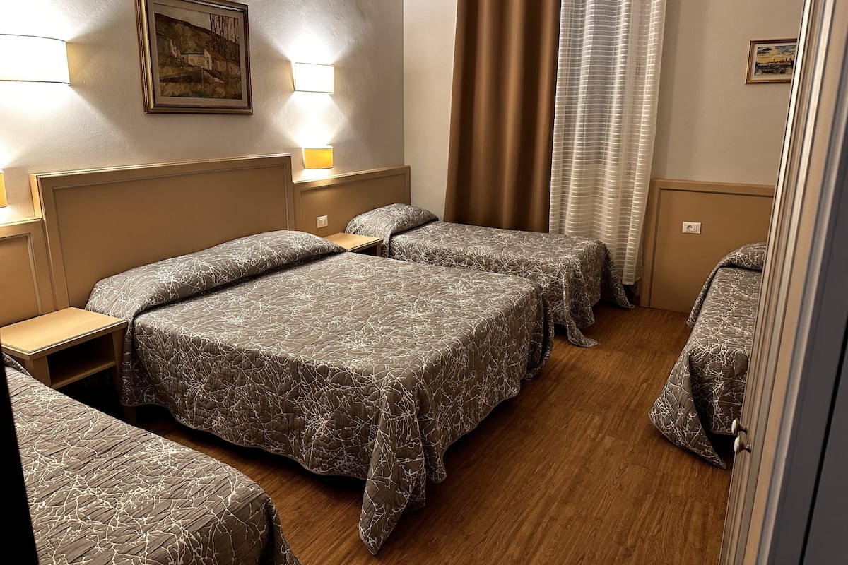 A hotel room with three beds, a wooden floor, and a painting on the wall.
