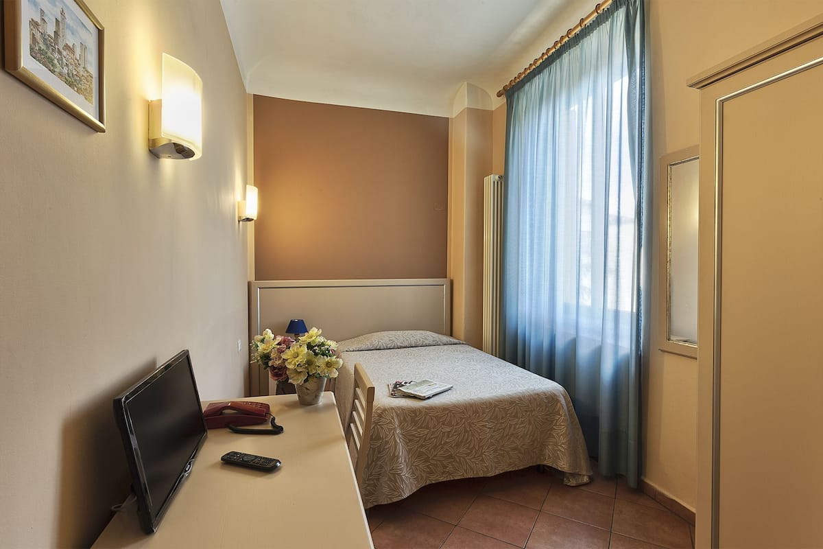 A hotel room with a bed, a desk with a laptop, a telephone, and a remote control.
