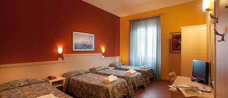 A hotel room with four beds, a television, a desk with a computer, and a window with curtains.