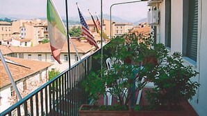 A balcony with flags, a view of buildings, and a plant. - Hotel Cordova (Florence)