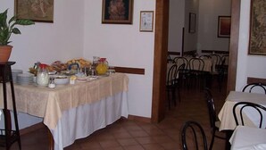A dining area with a table set for breakfast, including plates, glasses, and a variety of food items. There are chairs around the table, and the room has a tiled floor and walls adorned with framed pictures. - Hotel Cordova (Florence)