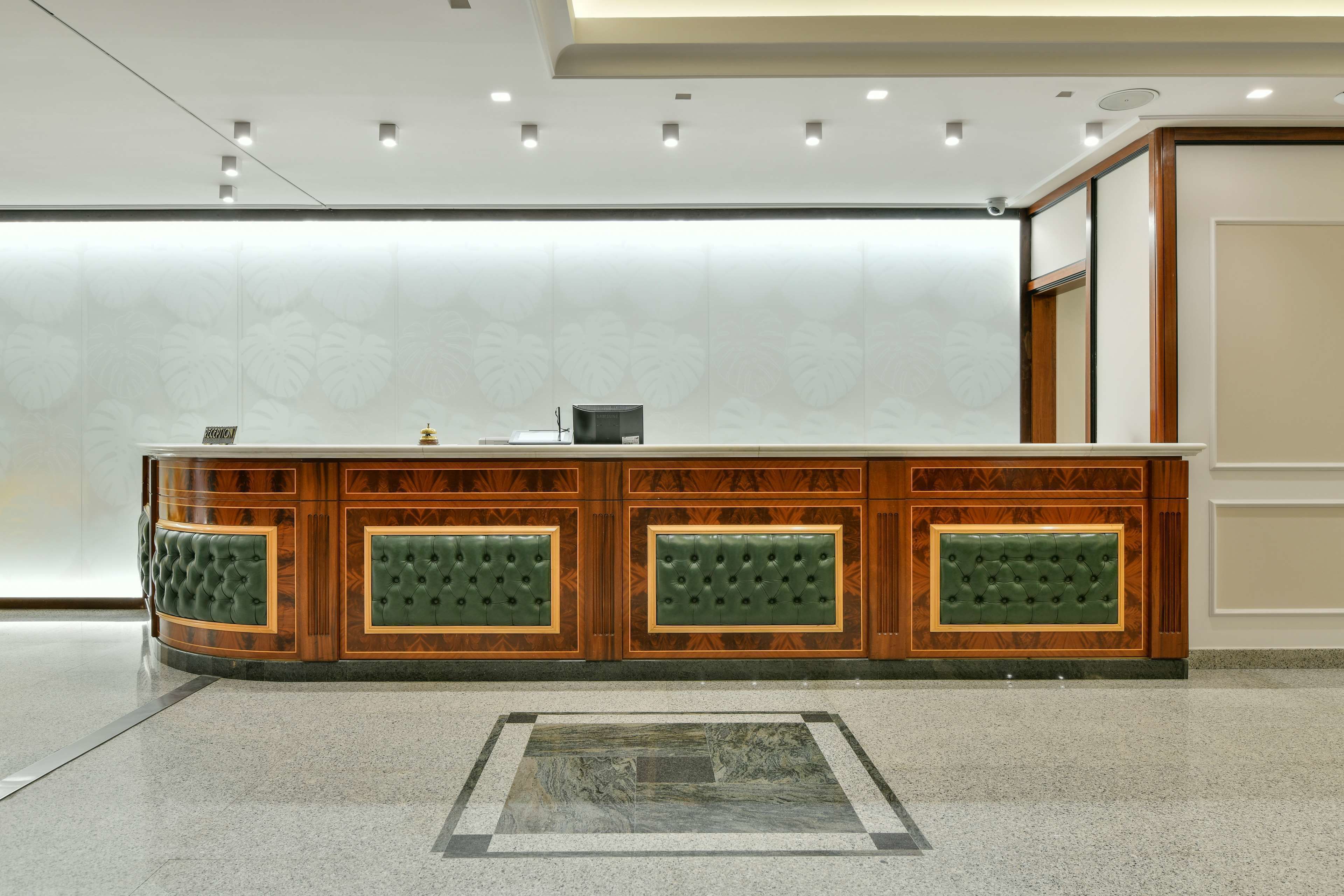 A reception area with a wooden counter, green cushioned panels, and a marble-patterned floor.