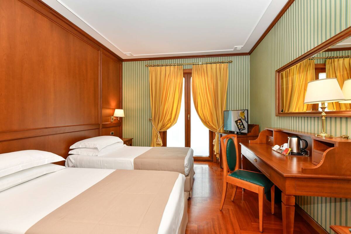 A hotel room with two beds, a desk, a chair, a mirror, and a window with curtains.