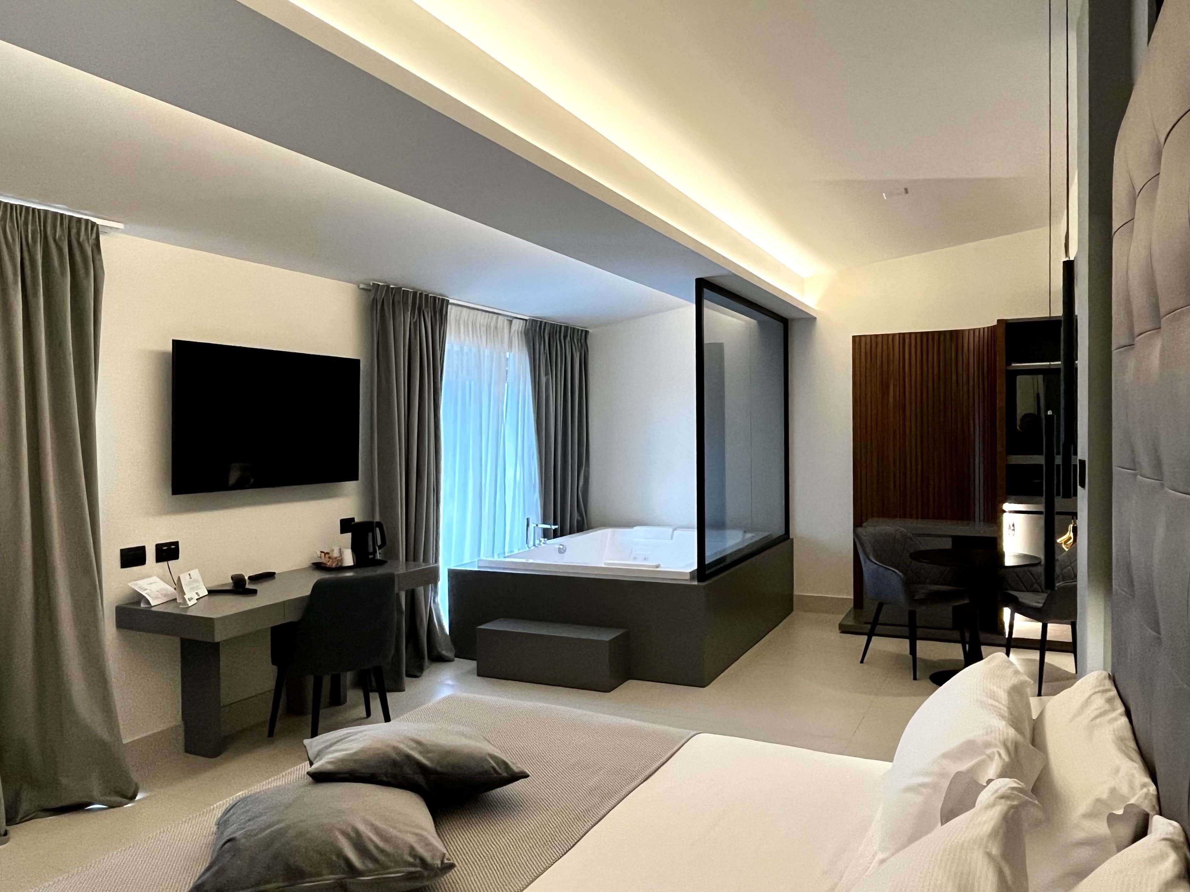 A modern hotel room with a bed, a desk, a TV, and a seating area.