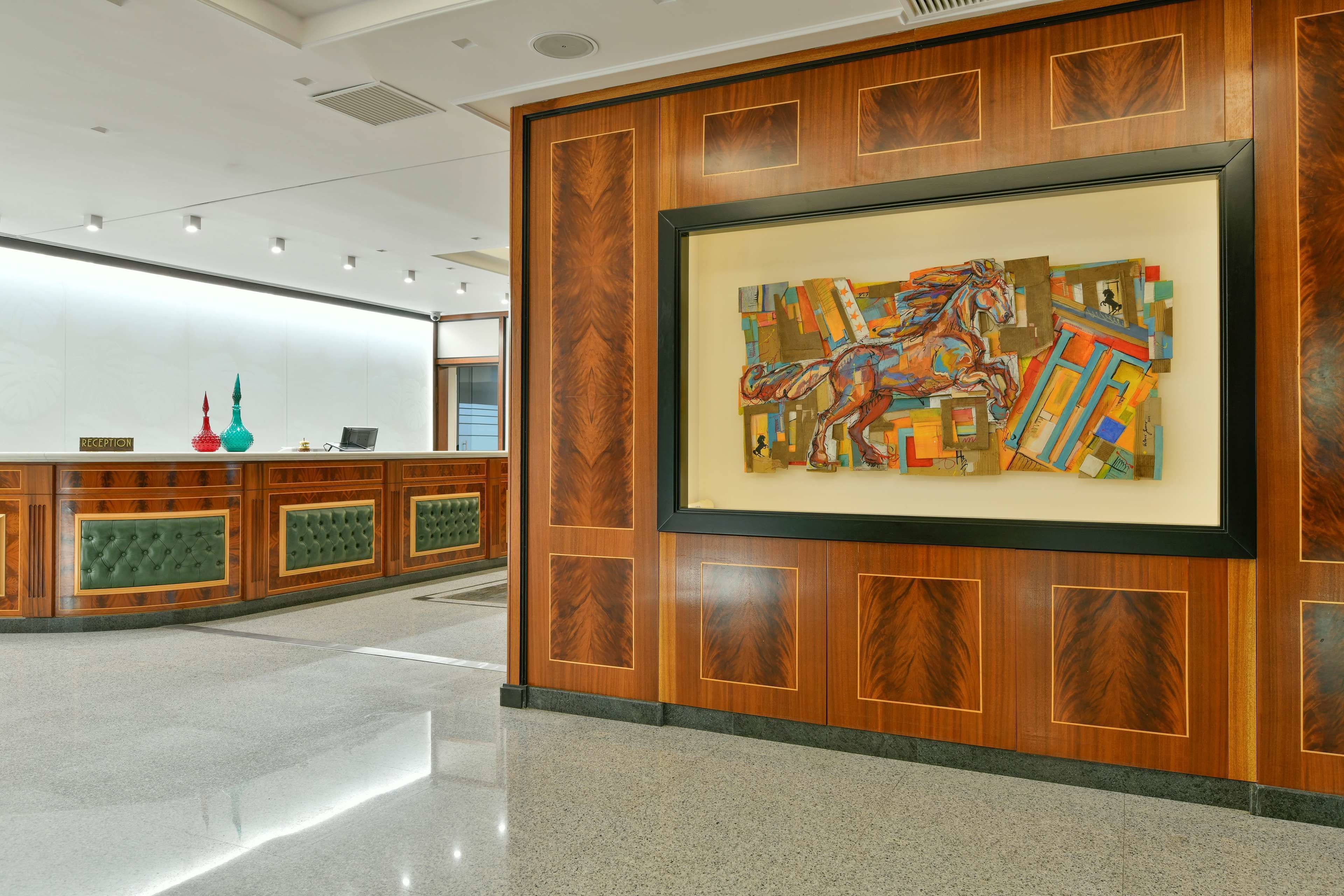 A reception area with a wooden panel design, a framed abstract painting, and a reception desk with a green cushioned backrest.