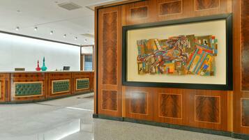A reception area with a wooden panel design, a framed abstract painting, and a reception desk with a green cushioned backrest.
