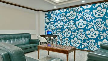 A modern living room with green leather sofas, a wooden coffee table, and a patterned blue and white wallpaper.