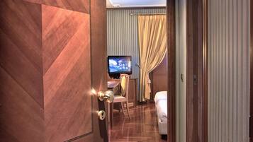 A hotel room with a wooden floor, a bed, a television, and a window with curtains.