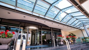 Une entrée moderne avec un hall surmonté d’une verrière, une porte tournante et des marches menant à un espace bar.