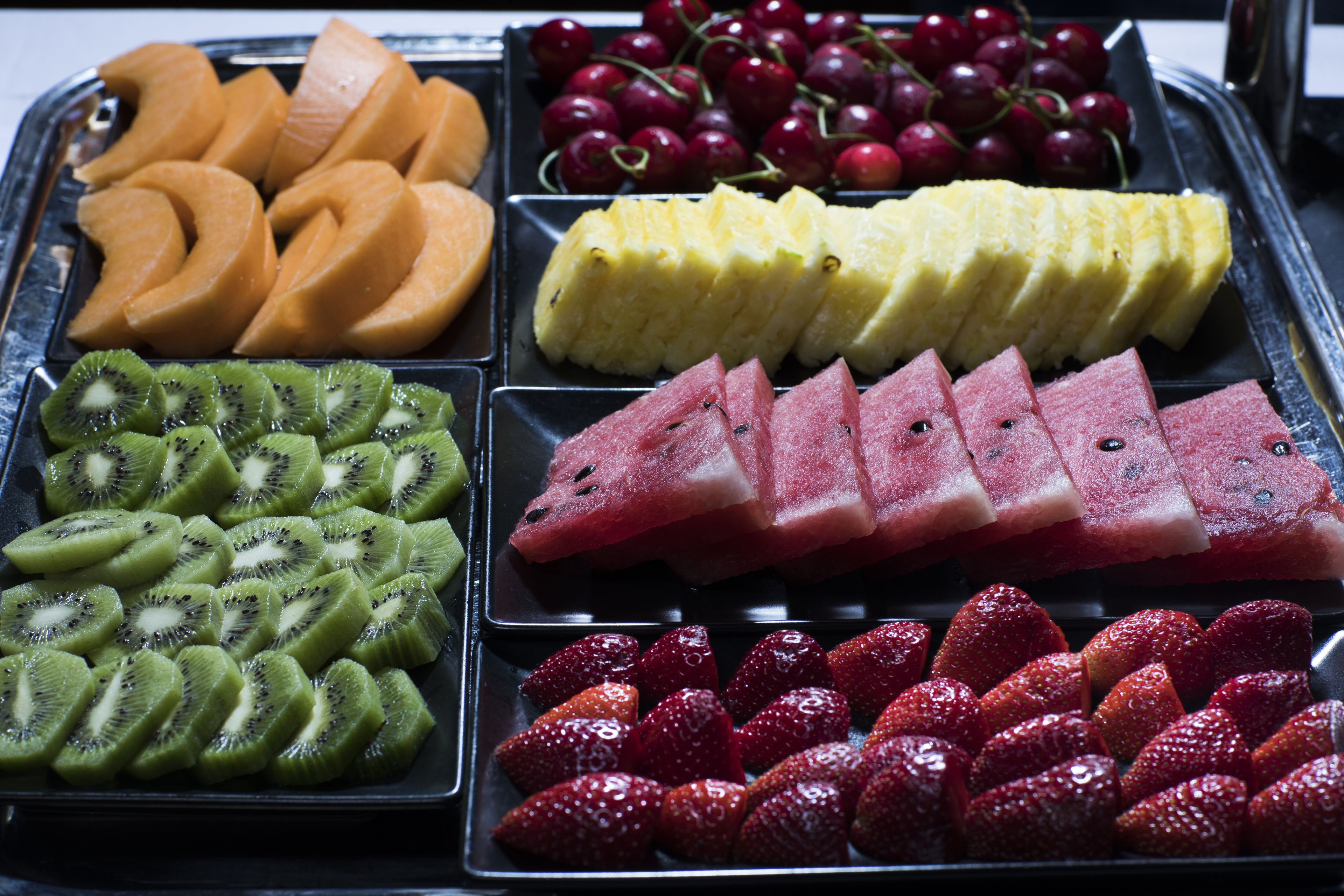 Un plateau contenant une variété de fruits, notamment des tranches de kiwi, de pastèque, des fraises, du melon, de l’ananas et des cerises.