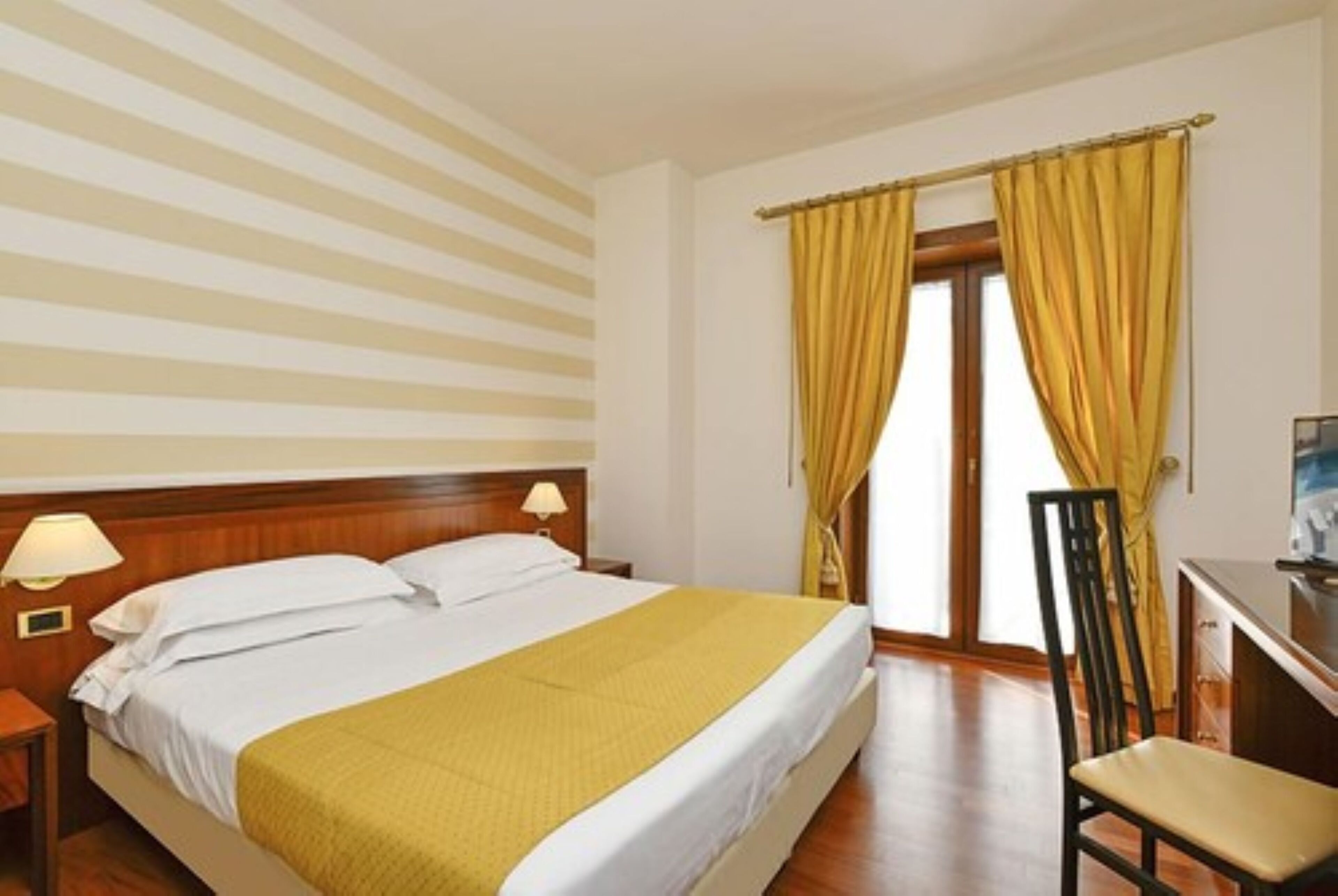 A hotel room with a bed, nightstands, a desk, and a chair.
