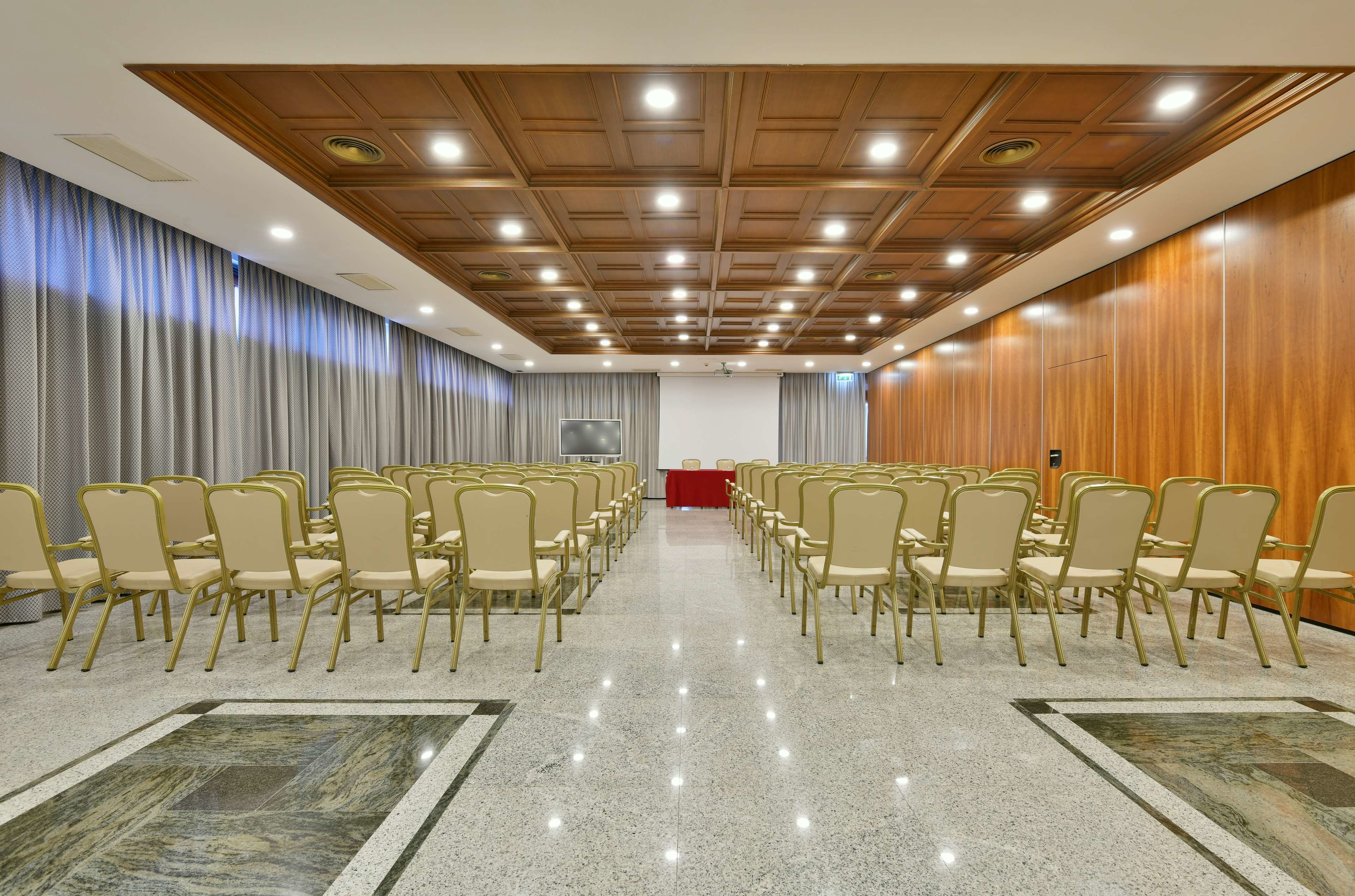 Una sala conferenze con file di sedie, un podio e un soffitto in legno con illuminazione a incasso.