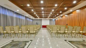 Una sala conferenze con file di sedie, un podio e un soffitto in legno con illuminazione a incasso.