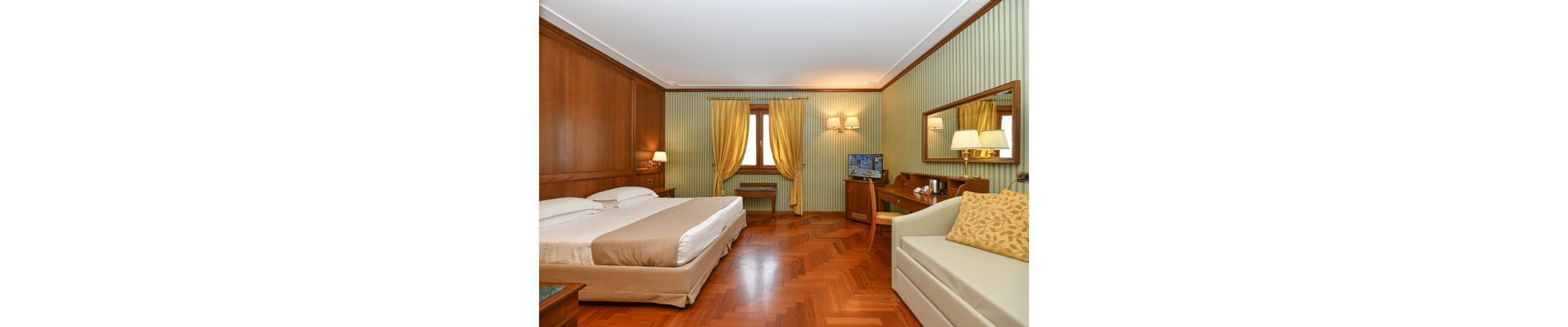 Une chambre d’hôtel avec deux lits, un canapé, une télévision et un miroir.