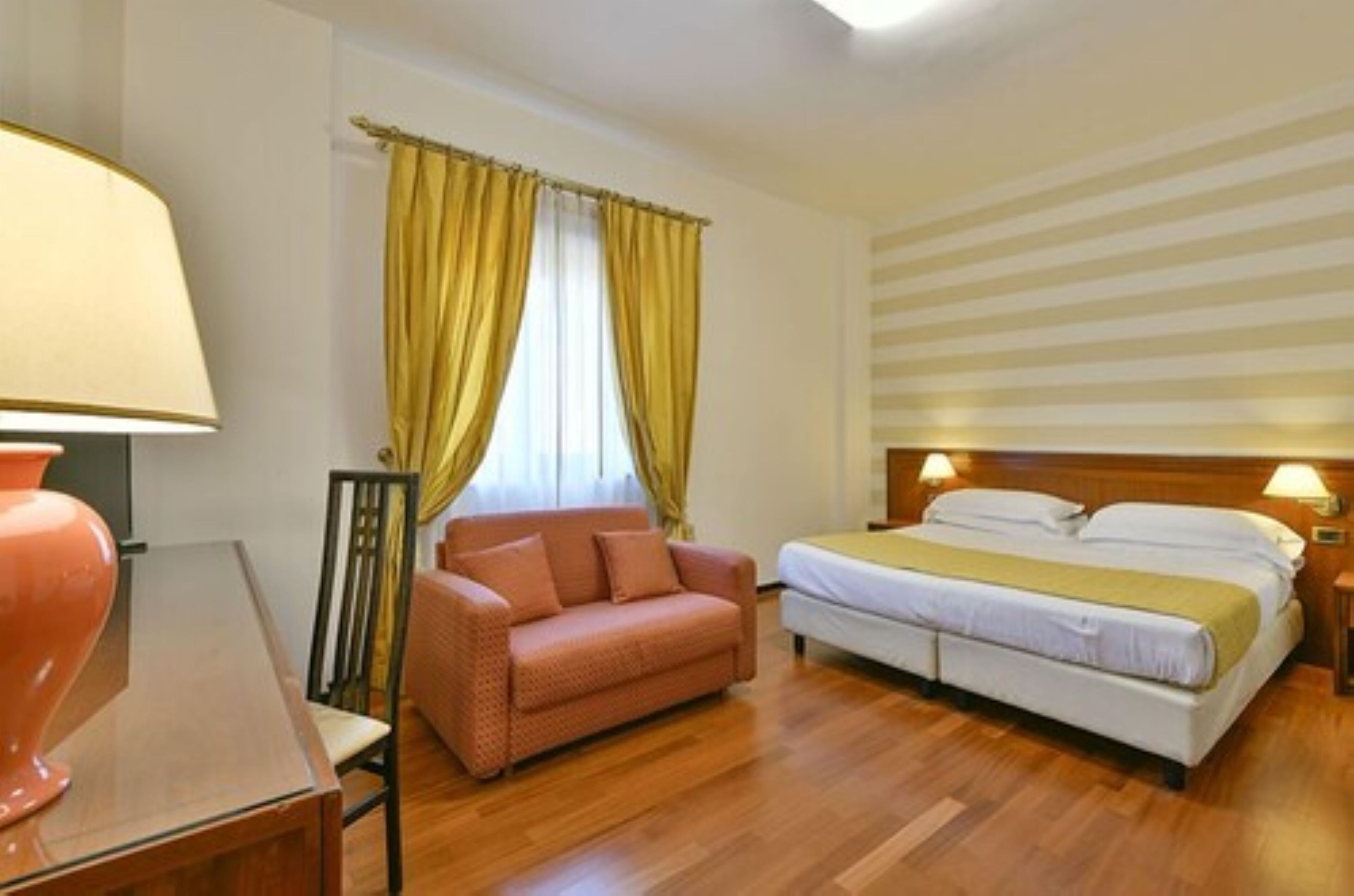 A hotel room with a bed, a sofa, a table, and a lamp.