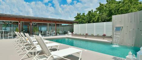 A swimming pool with lounge chairs and a waterfall feature.