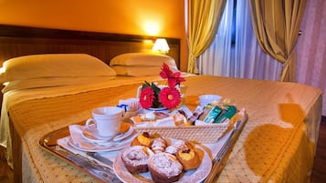 A neatly made bed with pillows, a tray with pastries, a cup, and a flower arrangement.